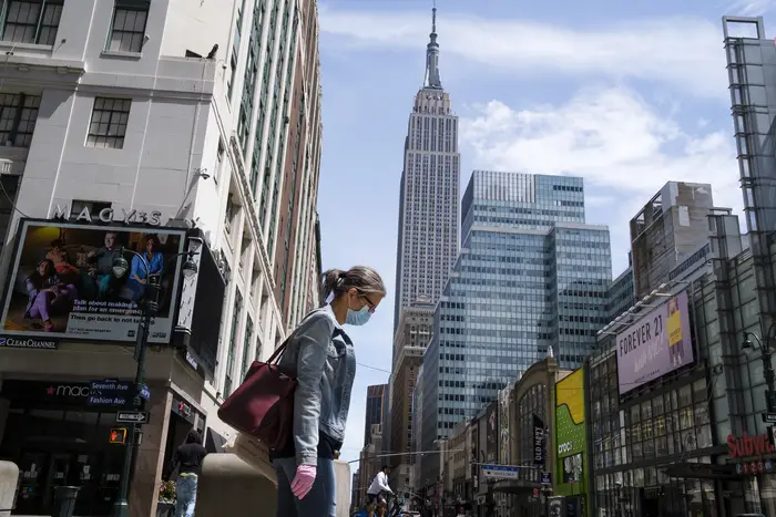A woman wearing a mask walks through a quiet midtown block in New York, with the Empire State Building in the background